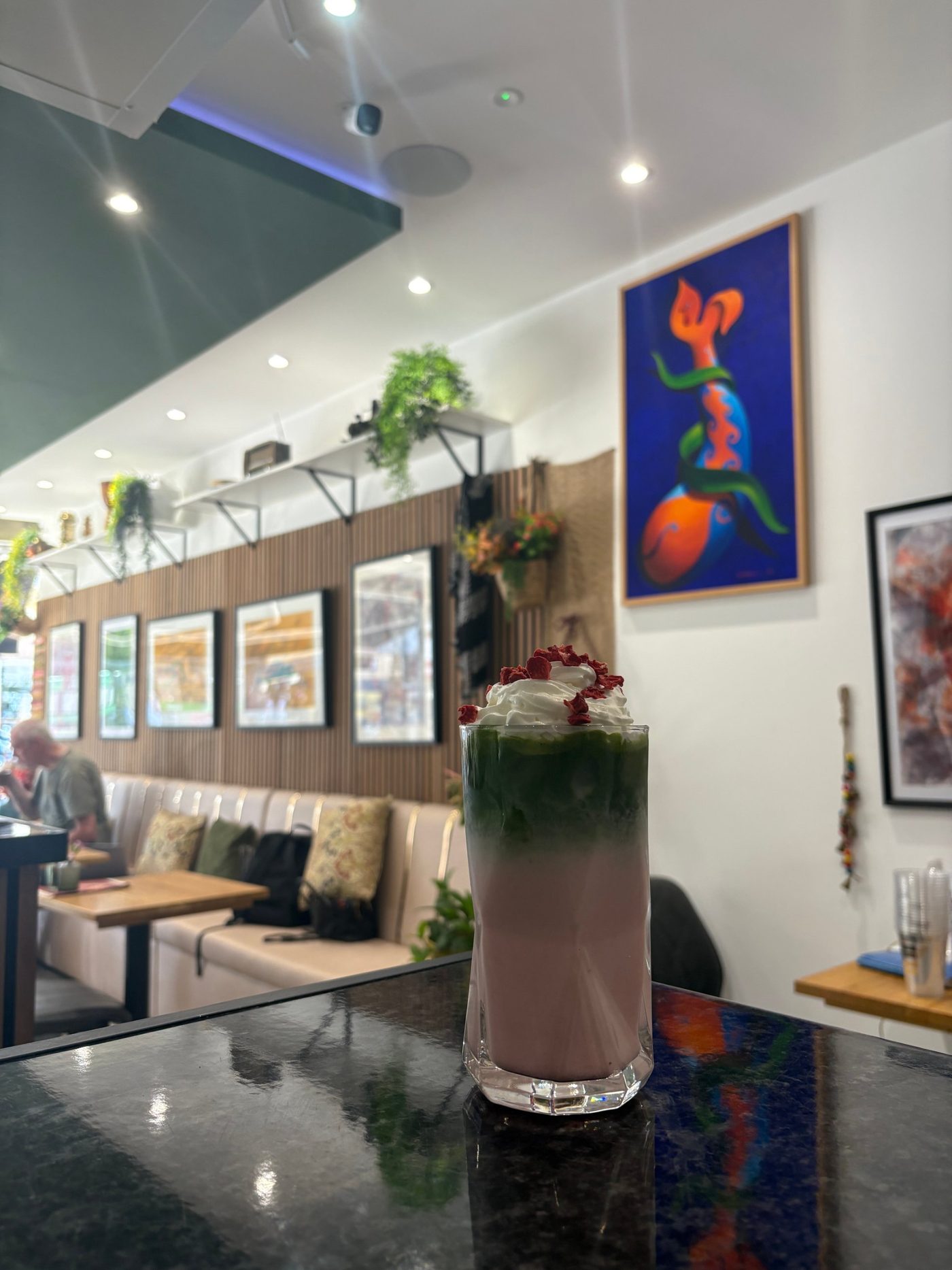 A strawberry matcha in front of Dad's paintings on the café walls